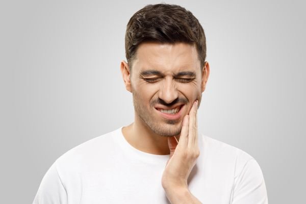man in white t shirt holding lower jaw | dentist los gatos ca