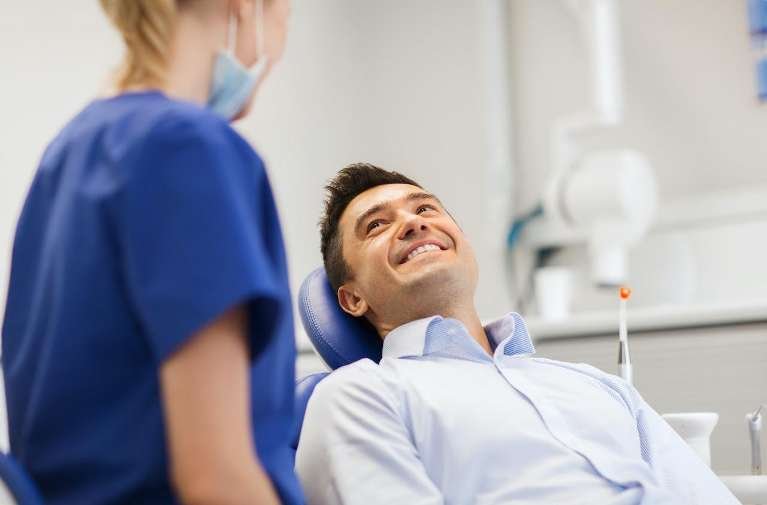 man sitting in dentist exam chair smiling | dental crowns los gatos